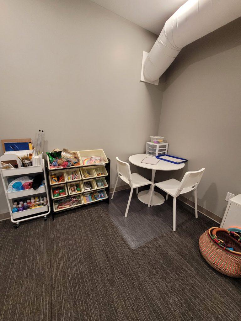 a small white table with two white chairs next to bins with activities for children