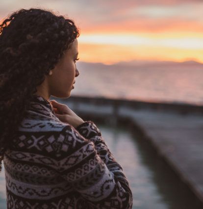 a woman standing on a dock looking out at a sunset over the water